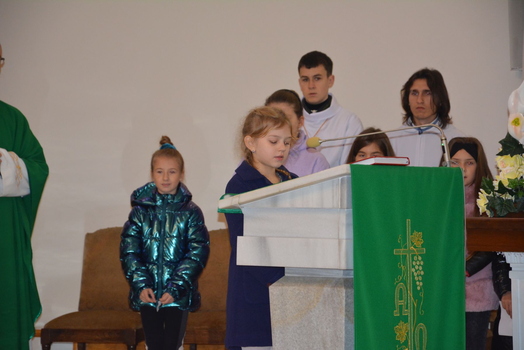Wnętrze kościoła, dziewczynka czyta z ambony, w tle inne dzieci oraz dwóch ministrantów