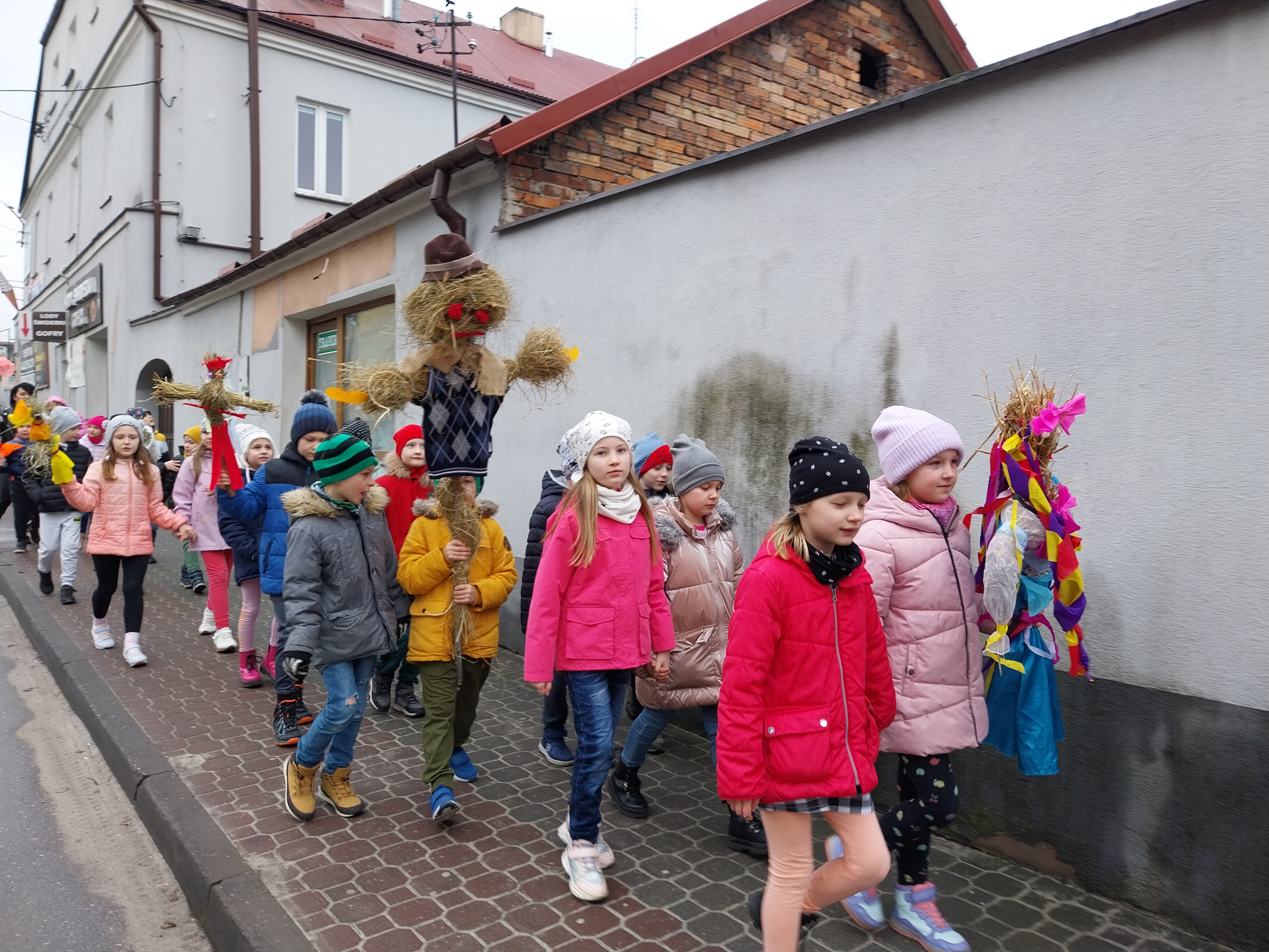 Grupa dzieci idzie ulicą niosąc marzanny