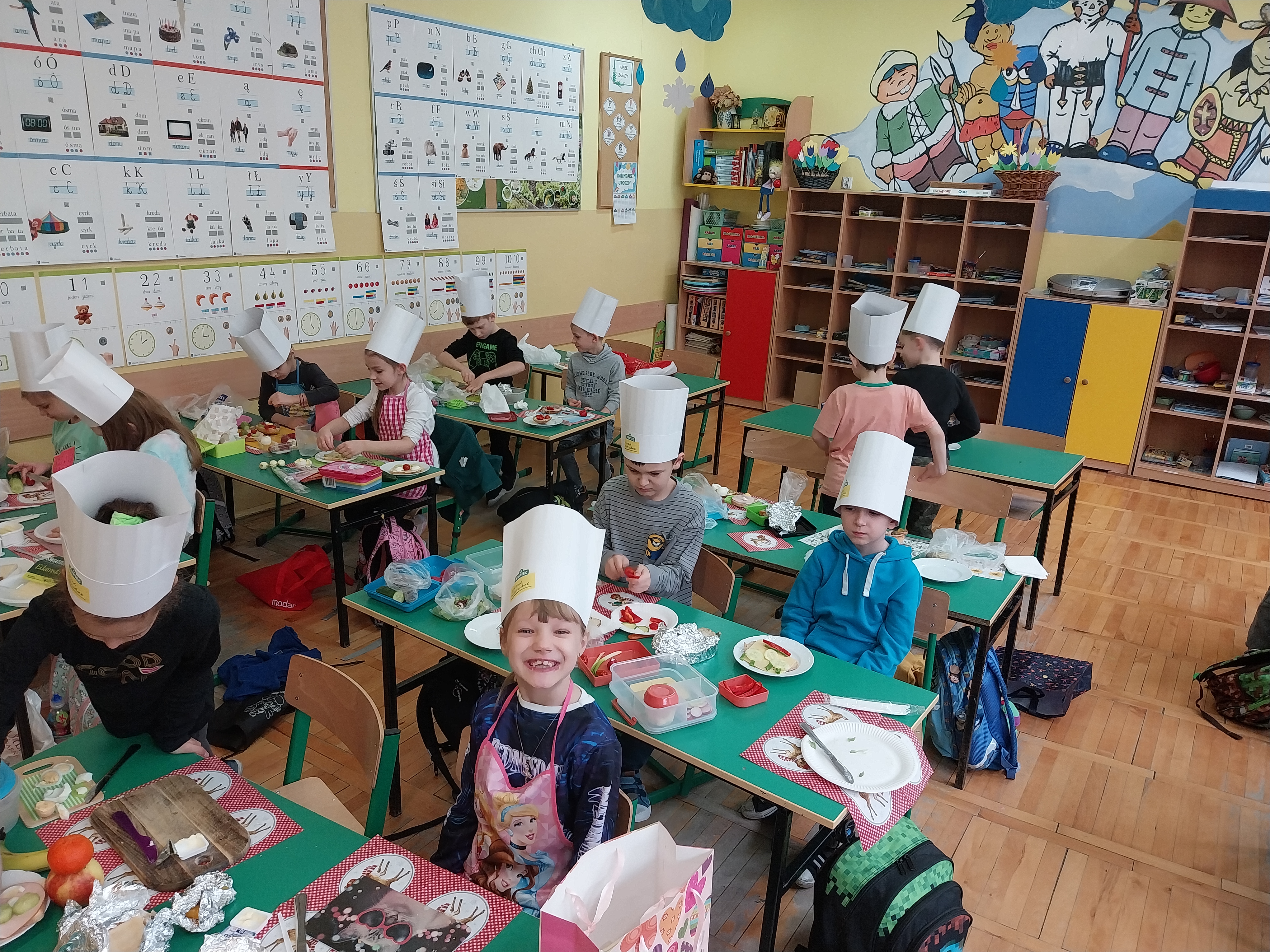 Dzieci w czapkach kucharskich przygotowują posiłek w sali lekcyjnej
