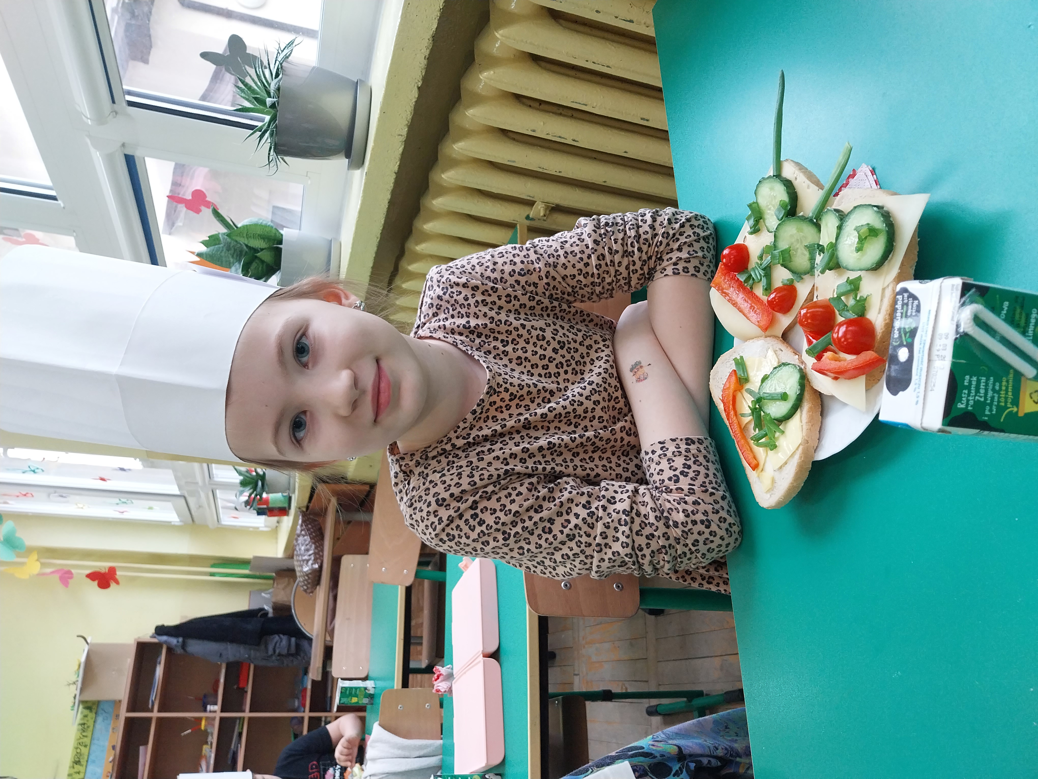 Dziewczynka w czapce kucharskiej siedzi przed talerzem z kanapkami