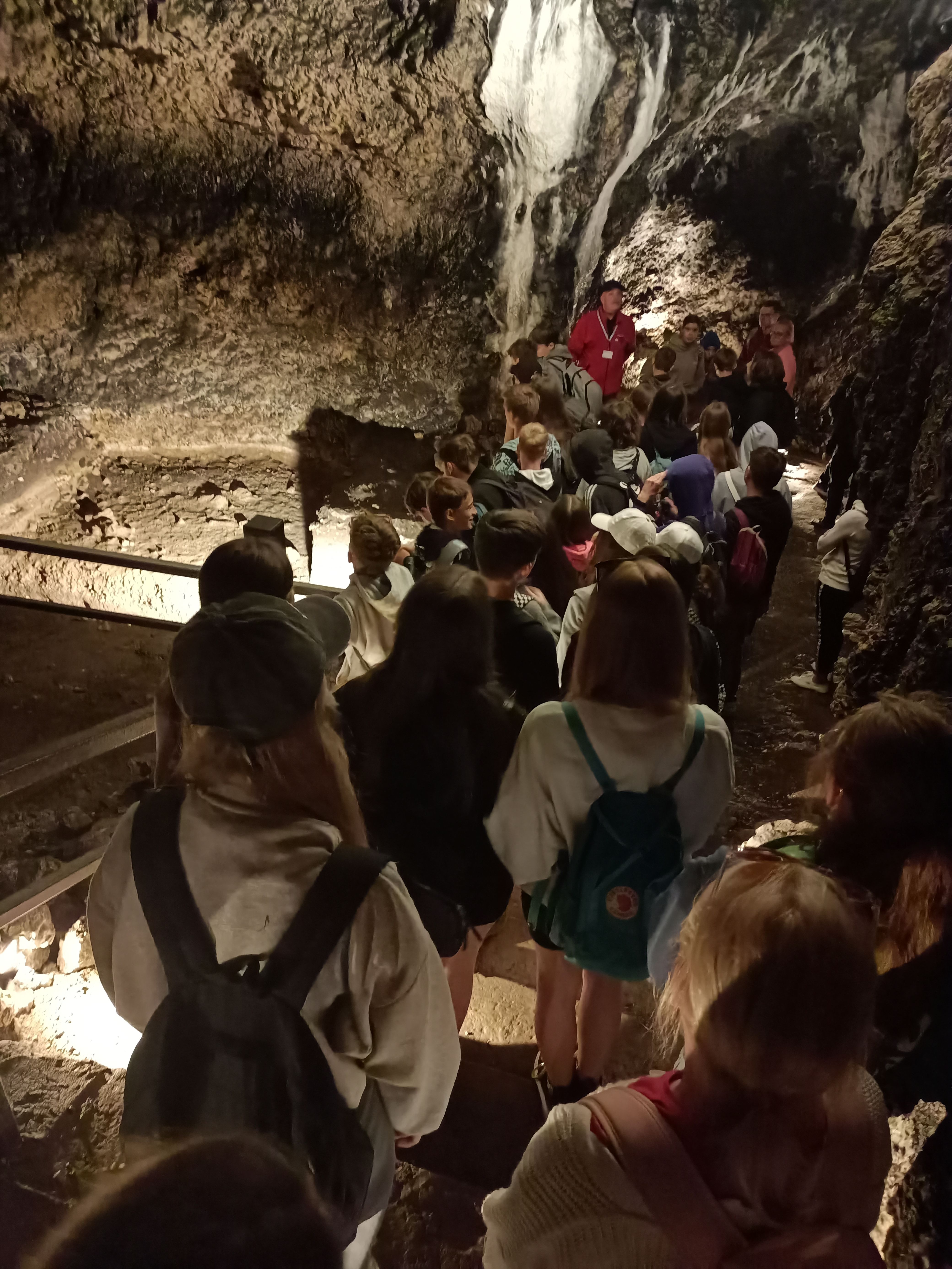 Uczniowie z zainteresowaniem słuchają opowiadania przewodnika w środku Jaskini Łokietka