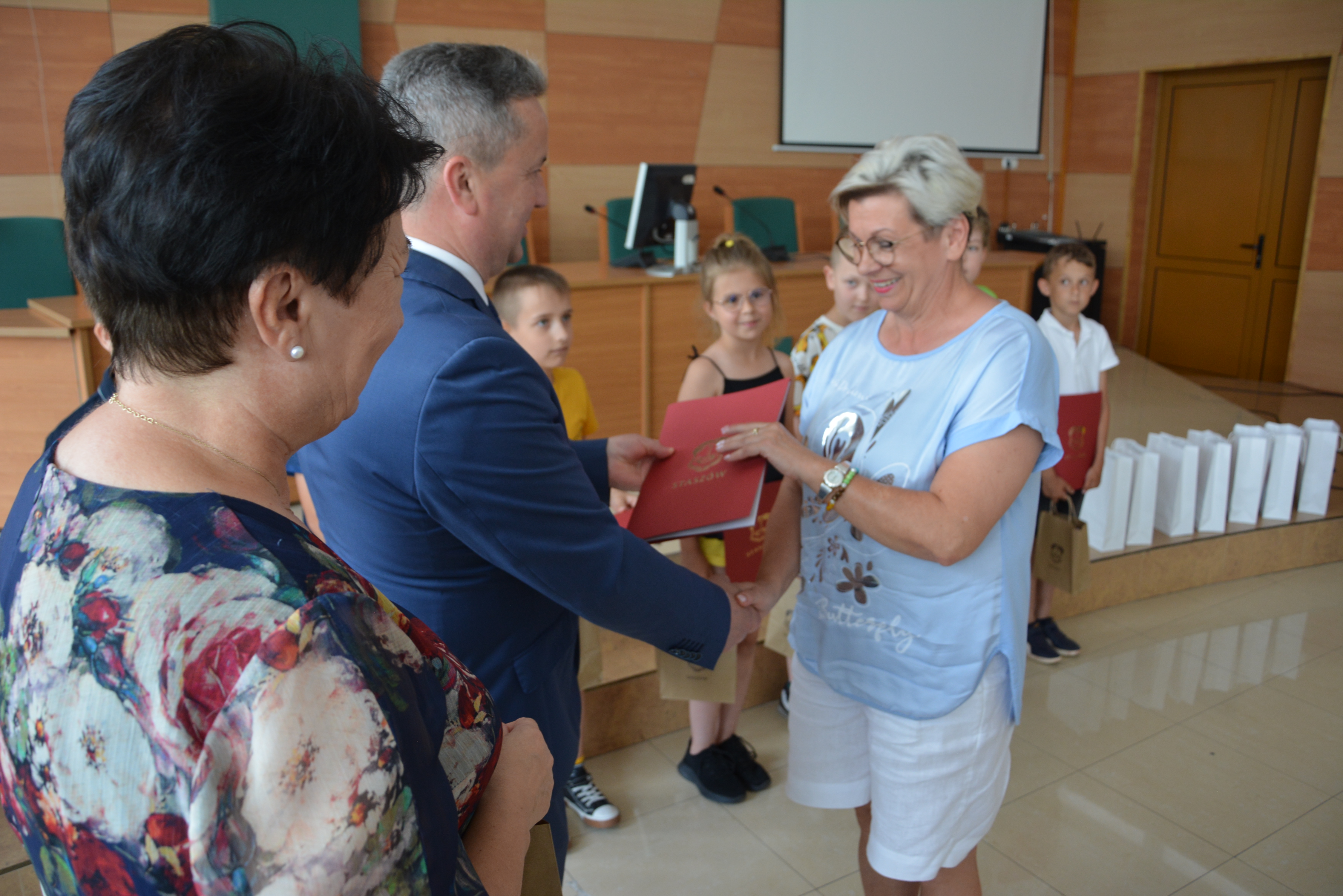 Nauczycielka odbiera dyplom i gratulacje od burmistrza i pani kierownik wydziału edukacji